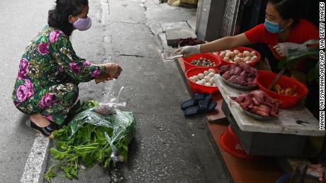 A woman applies social distance while shopping for groceries behind a line in a wet market in Hanoi.