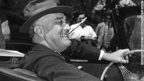 A smiling Franklin Delano Roosevelt, playfully sitting with a cigarette in a clenched teeth, sits at the wheel of his convertible, hot springs, Georgia, 1939. (Photo by Underwood Archives / Getty Images)